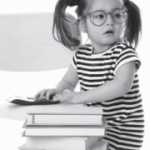 young girl with glasses next to a pile of books