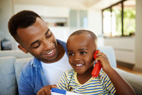 father holds son as he pretends to talk on toy phone