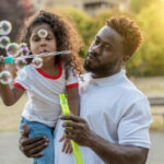 dad and girl blowing bubbles outdoors