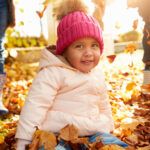 toddler in pink hat with fall leaves